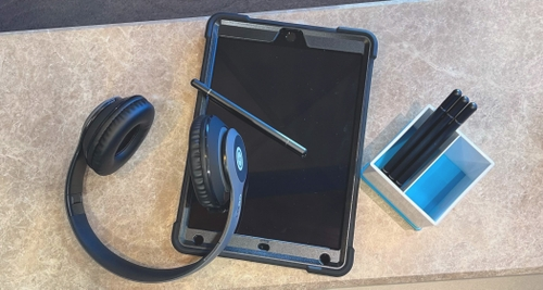 An Ipad, headphones, and pens are on a desk